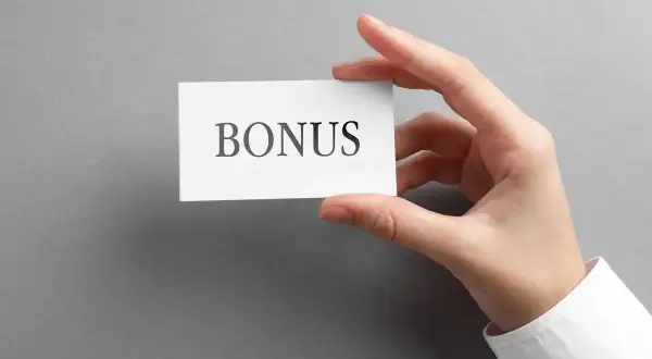 Dłoń trzyma kartkę z napisem "BONUS". To może być zapowiedź dodatku stażowego, który czeka na pracownika.