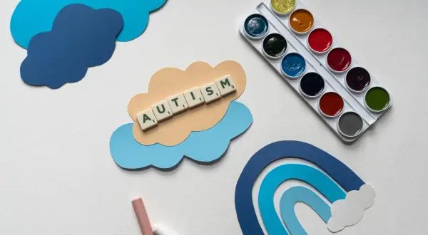Terapia dziecka z aspergerem w domu: chmurki, tęcza, kredki i farby. Słowo AUTISM ułożone z liter.