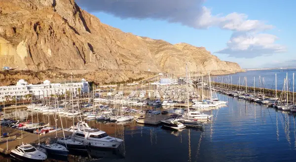 El puerto deportivo Aguadulce, con sus barcos amarrados y un hotel blanco, se extiende bajo una imponente montaña rocosa.