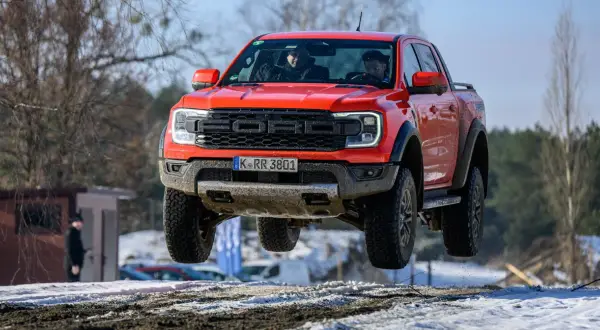 Czerwony Ford Raptor w locie nad śnieżnym terenem. Kierowcy w kabinie, a cena tego potwora budzi podziw.