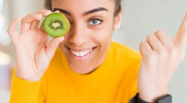 Junge Frau hält Kiwi vor ihr Auge, ein Symbol für gesunde Ernährung und eine gesunde Leber.