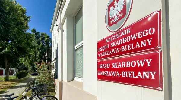 Tablice Urzędu Skarbowego Warszawa-Bielany. Obok stoją rowery, a w tle drzewa i błękitne niebo. sd-z2.