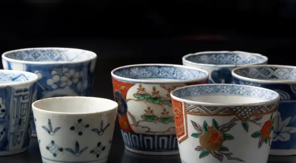 Vielfalt der japanischen Porzellankunst: Mehrere kleine Becher mit traditionellen Mustern, darunter Blumen und geometrische Formen, auf dunklem Hintergrund.