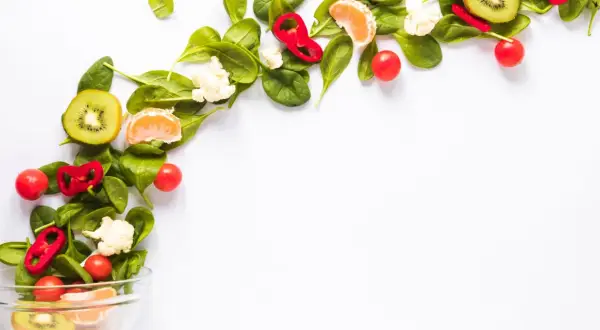 Kolorowe warzywa i owoce, takie jak kiwi, pomarańcza, papryka i pomidorki, tworzą kompozycję idealną dla diety wegańskiej.