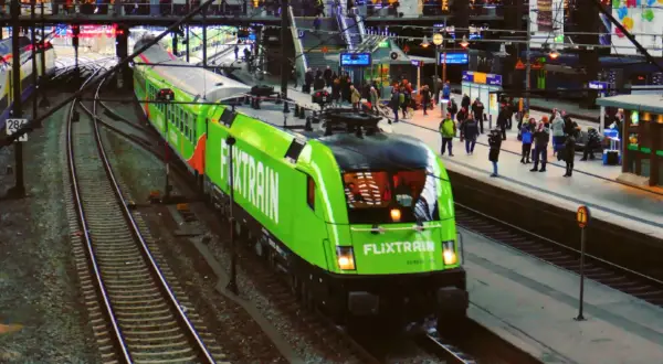 Ein grüner FlixTrain fährt in Berlin Hbf ein. Reisende warten auf dem Bahnsteig.