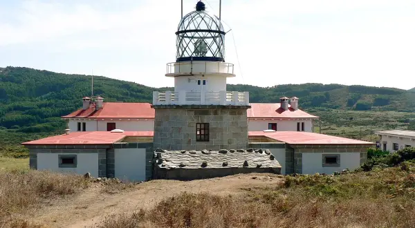 El faro de estaca de bares se alza imponente sobre la costa, con sus edificios blancos y tejados rojos rodeados de vegetación.