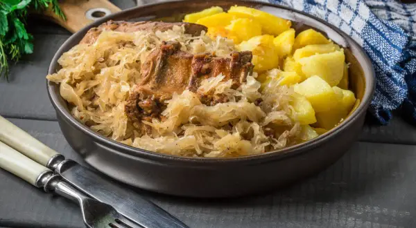 Pyszne żeberka w kapuście z ziemniakami, podane w misie. Obok sztućce i serwetka.