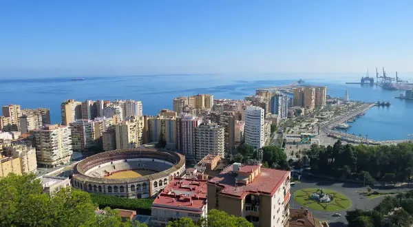Vista panorámica desde el mirador de Gibralfaro: la plaza de toros, el puerto y la ciudad de Málaga bajo un cielo azul.