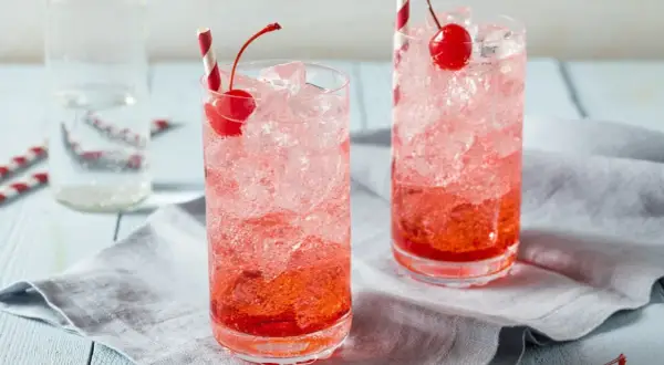 Erfrischende Crodino Rezepte: Zwei Gläser mit Eis, Kirschen und roten Strohhalmen.