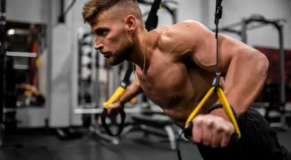 Mężczyzna wykonuje pompki z użyciem taśm TRX. Intensywny trening okluzyjny buduje siłę i masę mięśniową.