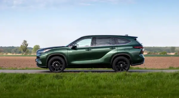 Zielony Toyota Highlander z czarnymi felgami stoi na tle pól i nieba.