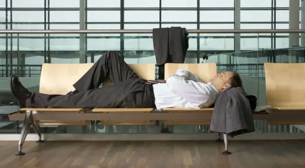 Biznesmen śpi na ławce w poczekalni lotniska, próbując pokonać jet lag. Ile trwa jet lag?