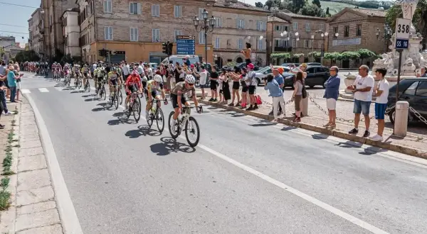 Ciclisti in gara durante il Giro d'Italia Marche, acclamati da spettatori festanti lungo la strada.