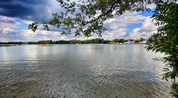 Spokojna tafla wody w Sobiborskim Parku Krajobrazowym, z widocznymi łódkami i karuzelą w oddali.