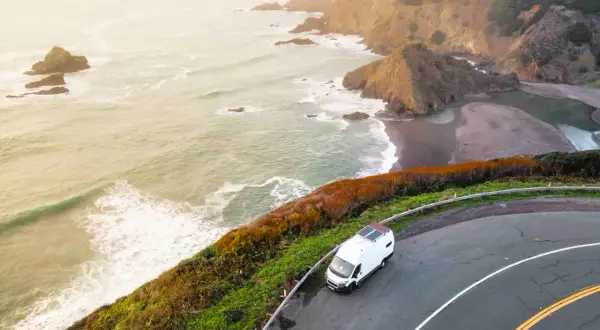 Biały kamper na krętej drodze wzdłuż wybrzeża Pacyfiku, idealny na road trip USA. Fale rozbijają się o skaliste klify.