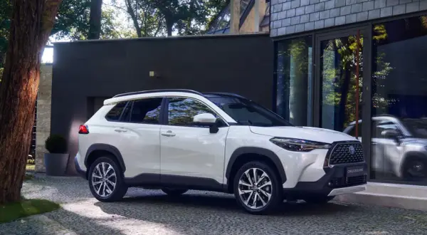 Biała Toyota Corolla Cross zaparkowana przed nowoczesnym budynkiem. Poznaj jej wymiary i możliwości.