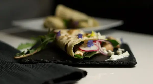 Ein gefüllter Wrap, der zeigt, was sind Tortillas: dünne Fladenbrote, gefüllt mit Hühnchen, Radieschen, Zwiebeln, Käse und Kräutern.