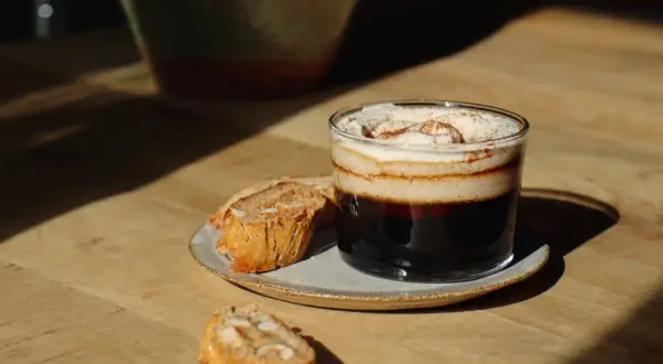 En lyxig kaffedrink med grädde och kanel, perfekt för att baka snabbt fika. Serveras med mandelkakor på ett fat.