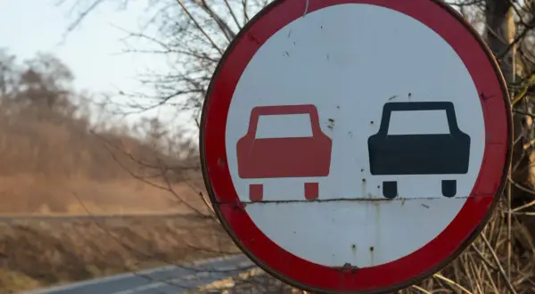 Znak drogowy informujący o końcu zakazu wyprzedzania. Dwa samochody, czerwony i czarny, symbolizują koniec ograniczenia.
