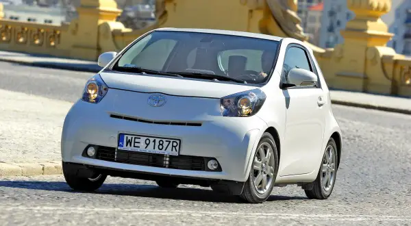 Biały, kompaktowy samochód Toyota iQ z polskimi tablicami WE 9187R jedzie po moście. Ten model, choć nie jest Daihatsu, oferuje podobną zwinność w mieście.