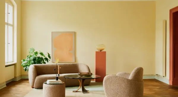 Ein Wohnzimmer mit gelben Wänden und einer grünen Decke, die frisch gestrichen wurde. Gemütliche Bouclé-Möbel laden zum Entspannen ein.