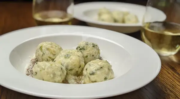 En tallrik med fluffiga gnudi, perfekt för ett enkelt gnudi recept. Serveras med riven ost och ett glas vitt vin.