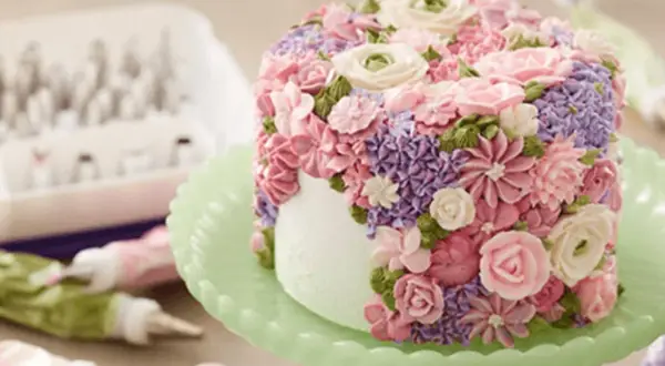 En tårta täckt av vackra blommor skapade genom att spritsa tårta med frosting i rosa, lila och gröna nyanser.