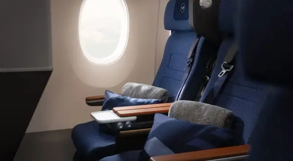 Lufthansa Premium Economy Sitze mit Kissen und Decken neben einem Fenster.