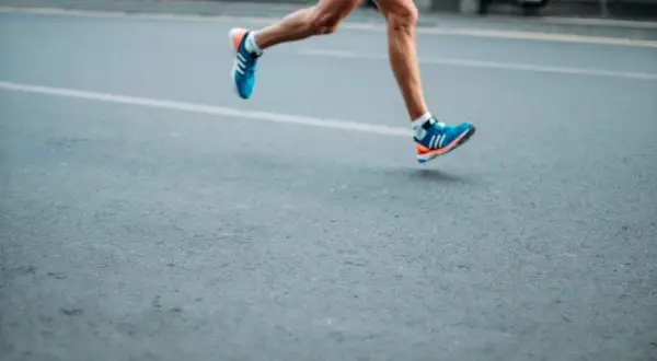 A runner's legs in motion, wearing blue and orange sneakers. This image evokes the dedication required to train, making one wonder how many miles do boxers run to achieve peak fitness.