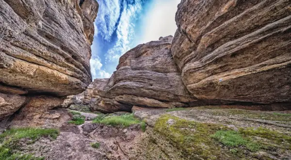 Sendero entre imponentes rocas erosionadas, con el cielo azul y nubes blancas asomando. Un paisaje que evoca la grandeza de los Picos de Urbión.