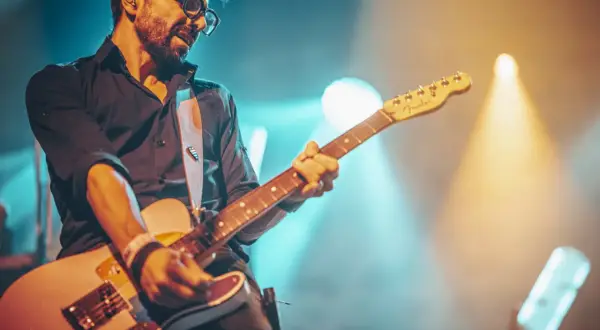 Muzyk w okularach gra na gitarze, otoczony światłami sceny. Jego gra to prawdziwa **farben lehre** dźwięków i emocji.
