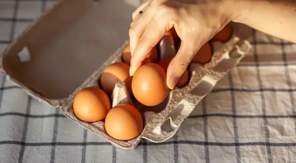 Dłoń wybiera jajko z wytłaczanki na kratkowanym obrusie.