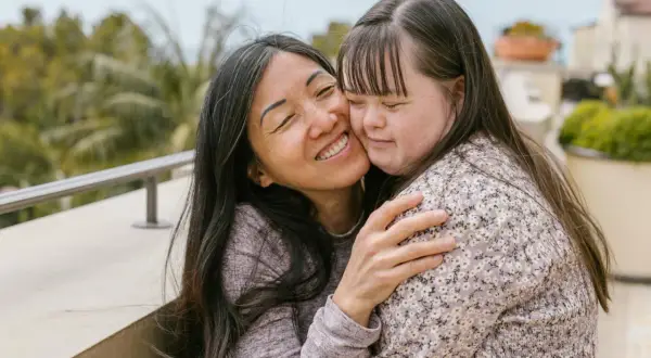 Abbraccio affettuoso tra due donne, una con sindrome di Down, che condividono un momento di gioia e amore.