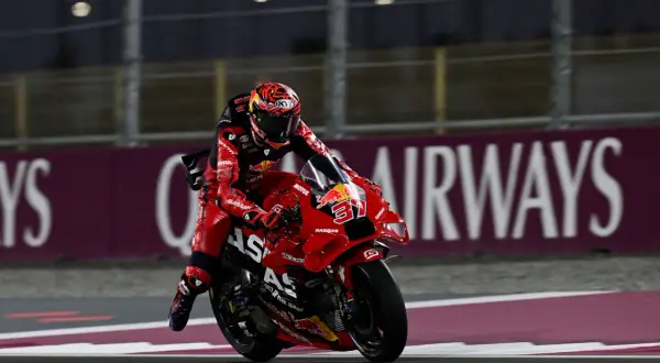 Piloto de MotoGP con traje rojo y casco a juego, en plena carrera. Busca sumar puntos en la clasificación.
