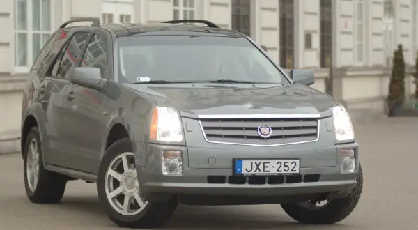 Szary Cadillac SRX z tablicą rejestracyjną JXE-252 zaparkowany przed budynkiem.