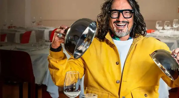 Chef con giacca gialla solleva un coperchio, pronto a svelare un piatto in un ristorante. Un assaggio di "4 ristoranti".