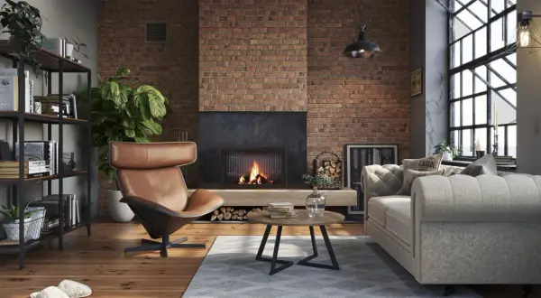Przytulny, **soft loft** z ceglaną ścianą, palącym się kominkiem, wygodną kanapą i fotelem.