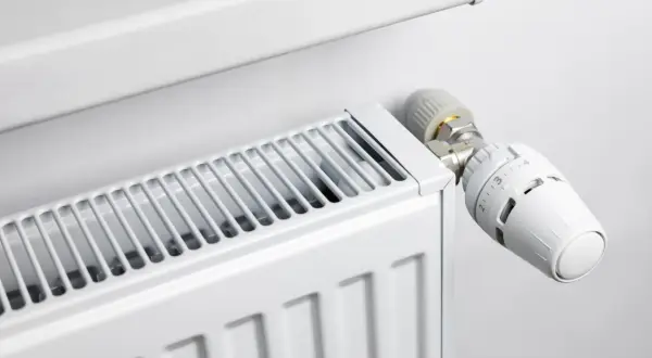 Biały grzejnik z widoczną głowicą termostatyczną, która pozwala regulować temperaturę. Różne rodzaje głowic termostatycznych zapewniają komfort cieplny.