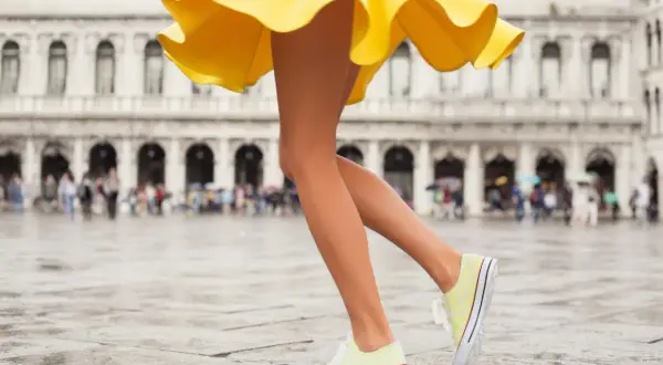 Nogi w żółtej sukience i stylowe buty sportowe do sukienki na mokrym placu w Wenecji.