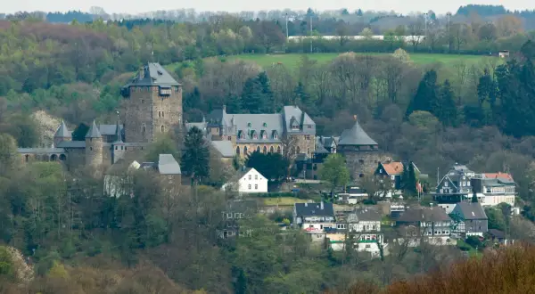 Zamek Schloss Burg w Solingen, otoczony zielenią, z wieżami i budynkami mieszkalnymi u podnóża.