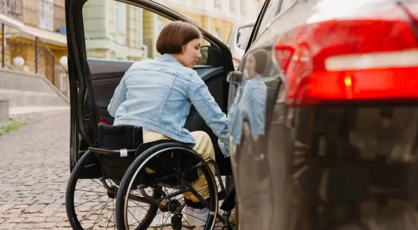 Donna in carrozzina si avvicina all'auto. Scopri lo sconto assicurazione auto legge 104 per una maggiore libertà di movimento.