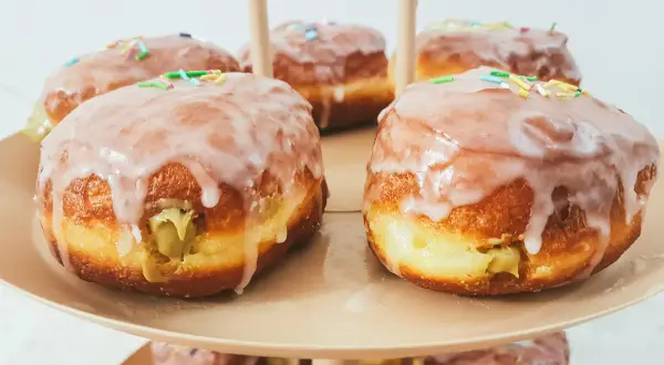Pyszne pączki pistacjowe z lukrem i kolorową posypką, ułożone na paterze.