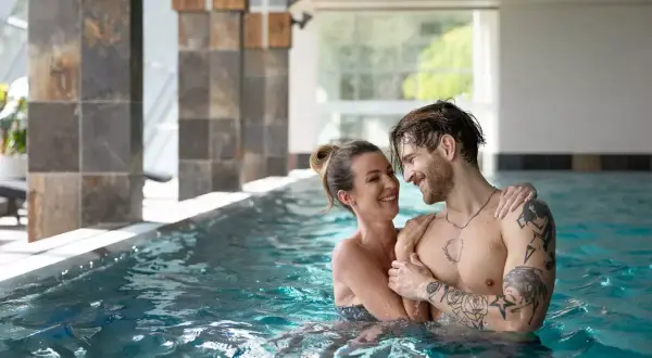 Para w basenie SPA, uśmiechnięci, patrzą na siebie.