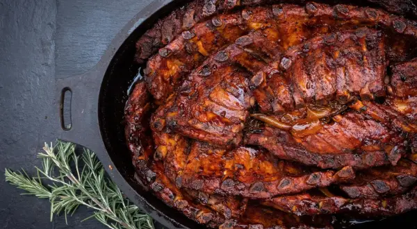 Saftige spareribs im Dutch Oven, glasiert und bereit zum Genießen. Ein Rosmarinzweig liegt daneben.