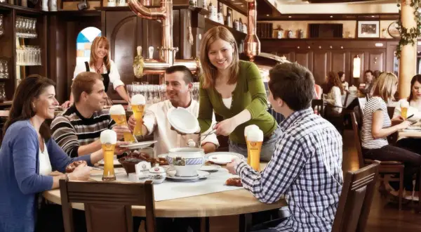 Gäste genießen Bier und Essen im Erdinger Brauhaus. Eine Kellnerin serviert, während Freunde lachen und trinken.