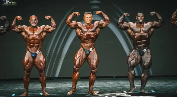 Drei Bodybuilder präsentieren ihre Muskeln auf der Bühne. Man fragt sich, wann ist Mr. Olympia?