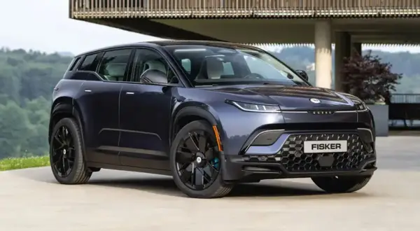 Fisker Ocean, un SUV eléctrico azul oscuro, aparcado frente a una casa moderna con vistas a un bosque.