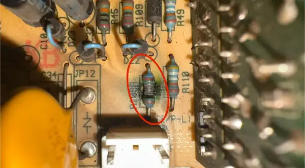 Uszkodzony rezystor z czerwonym okręgiem, otoczony innymi elementami elektronicznymi na płytce drukowanej.