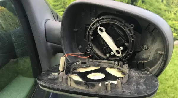 Rozmontowane lusterko zewnętrzne samochodu, gotowe do wymiany. Widać mechanizm regulacji i przewody.