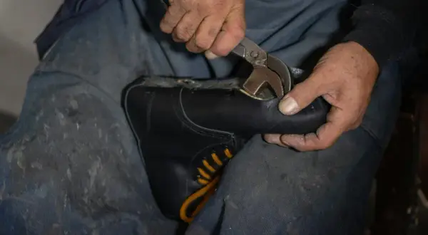 Mains d'un cordonnier travaillant sur une chaussure simili cuir qui s'effrite, utilisant une pince pour la réparer.